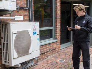 Energy assessor standing next to an air source heat pump recording notes about the heating source of a building in order to conduct an energy assessment