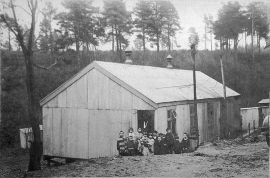 Corrugated iron building of Hurtwood Gypsy School with children outside