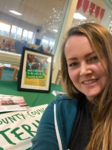 Photo of table with fostering items and smiling social worker at The Hive community hub in Guildford